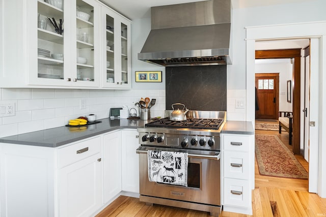 kitchen featuring high end stove, white cabinetry, backsplash, wall chimney exhaust hood, and light hardwood / wood-style flooring