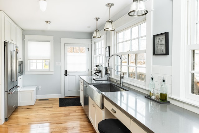 kitchen featuring sink, white cabinetry, hanging light fixtures, appliances with stainless steel finishes, and light hardwood / wood-style floors