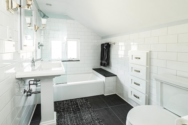 bathroom featuring tiled shower / bath, lofted ceiling, tile walls, toilet, and tile patterned floors