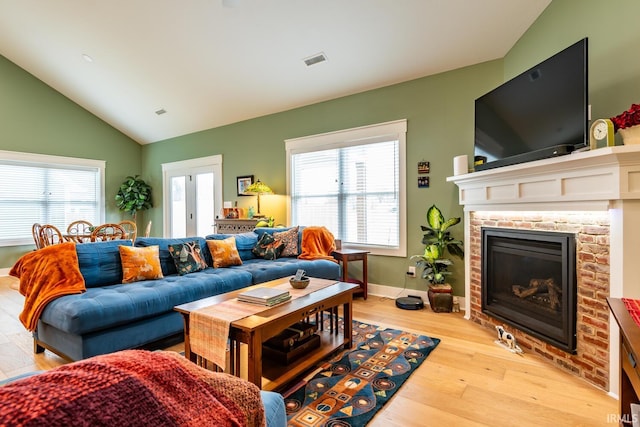 living room with vaulted ceiling, a fireplace, and light hardwood / wood-style floors