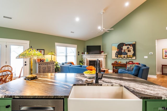 kitchen with high vaulted ceiling, a fireplace, sink, hardwood / wood-style flooring, and a kitchen island with sink