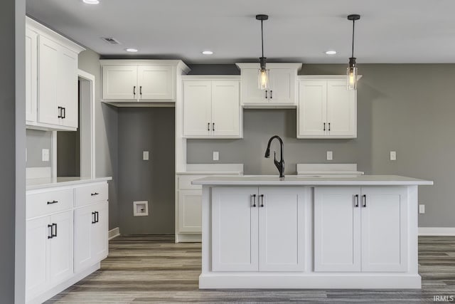 kitchen with wood-type flooring, pendant lighting, a center island with sink, and white cabinets