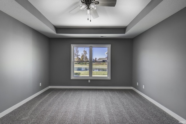 spare room with a raised ceiling, carpet floors, and ceiling fan