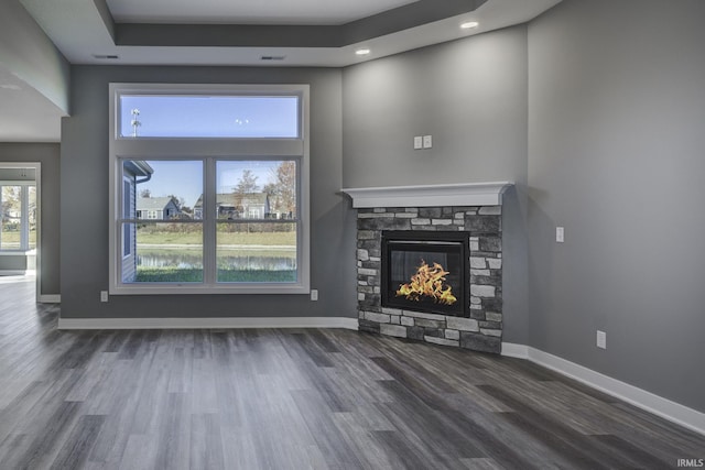 unfurnished living room with a high ceiling, a stone fireplace, dark hardwood / wood-style floors, and a tray ceiling