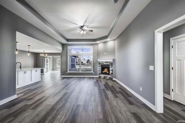 unfurnished living room featuring a tray ceiling, a fireplace, dark hardwood / wood-style flooring, and ceiling fan with notable chandelier