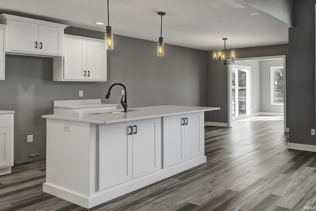 kitchen featuring sink, a kitchen island with sink, pendant lighting, and white cabinets