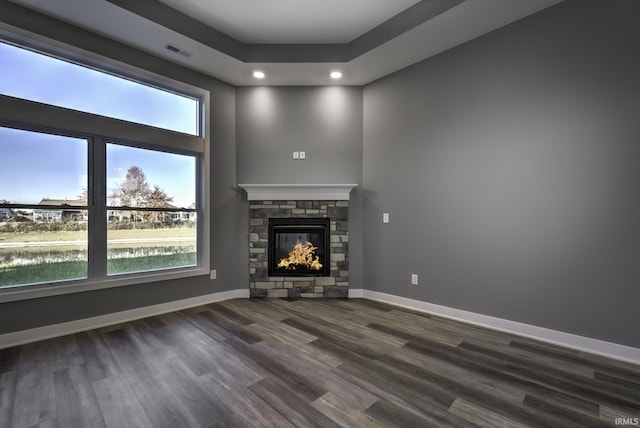 unfurnished living room featuring a tray ceiling, a stone fireplace, dark wood-type flooring, and a water view