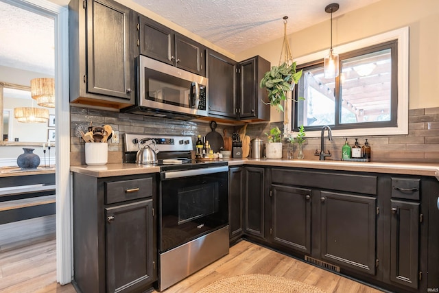 kitchen featuring sink, stainless steel appliances, a textured ceiling, decorative light fixtures, and light wood-type flooring