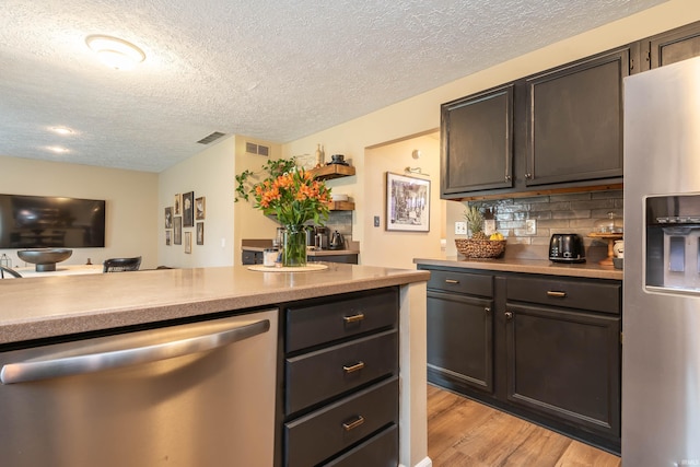 kitchen featuring dark brown cabinetry, a textured ceiling, light hardwood / wood-style flooring, appliances with stainless steel finishes, and backsplash