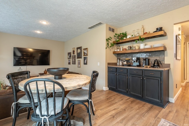 dining area with indoor bar, light hardwood / wood-style flooring, and a textured ceiling