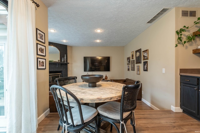 dining area featuring a fireplace, a textured ceiling, and light wood-type flooring