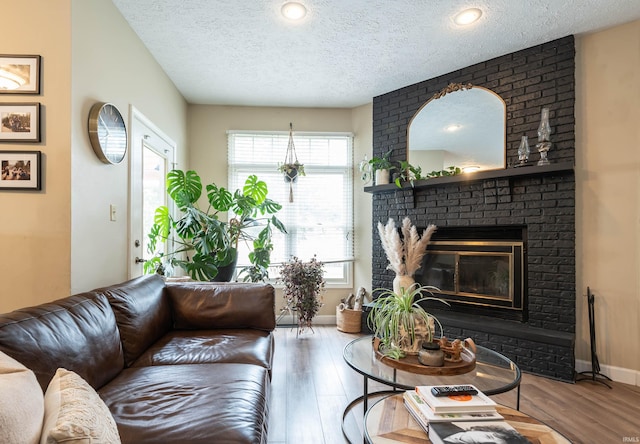 living room with hardwood / wood-style flooring, a brick fireplace, and a textured ceiling