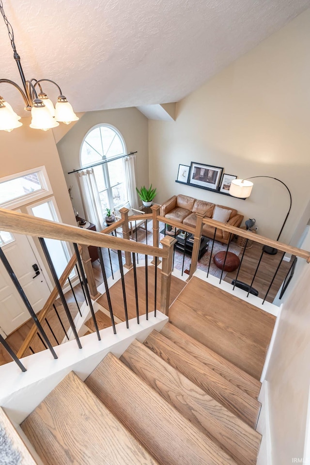 stairs featuring hardwood / wood-style flooring, lofted ceiling, a textured ceiling, and a chandelier