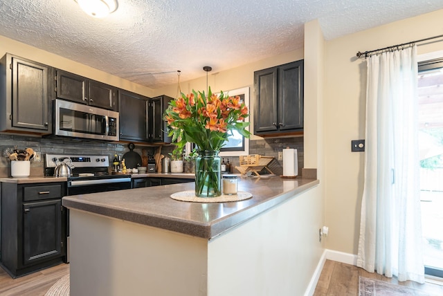 kitchen with hanging light fixtures, light wood-type flooring, appliances with stainless steel finishes, kitchen peninsula, and backsplash