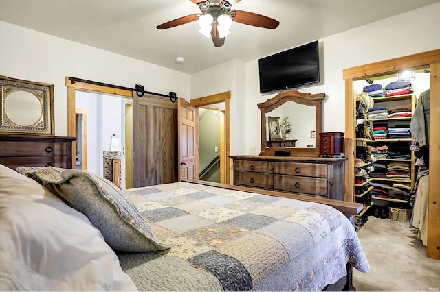 carpeted bedroom featuring ceiling fan, a walk in closet, a barn door, and a closet