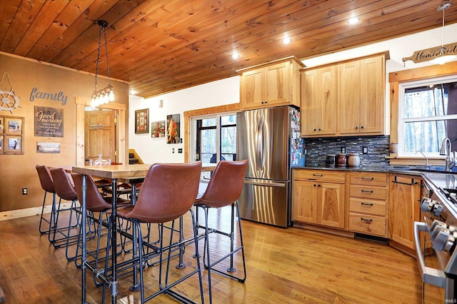 kitchen with light brown cabinetry, decorative light fixtures, a breakfast bar area, wood ceiling, and stainless steel appliances