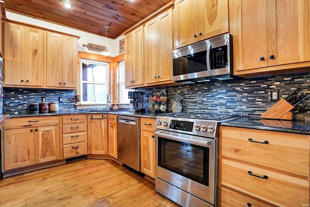 kitchen with sink, dark stone countertops, backsplash, light hardwood / wood-style floors, and stainless steel appliances