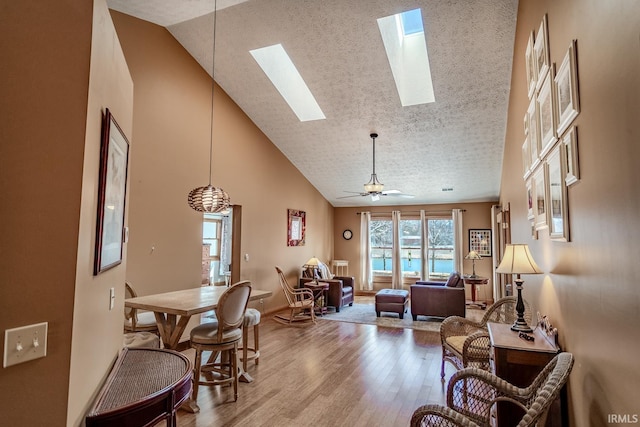 dining room with ceiling fan, light hardwood / wood-style flooring, high vaulted ceiling, and a textured ceiling