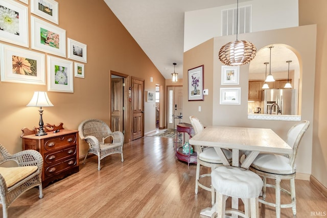 dining room featuring high vaulted ceiling and light hardwood / wood-style flooring