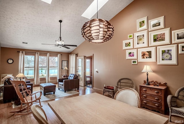 dining area with ceiling fan, lofted ceiling with skylight, light hardwood / wood-style flooring, and a textured ceiling