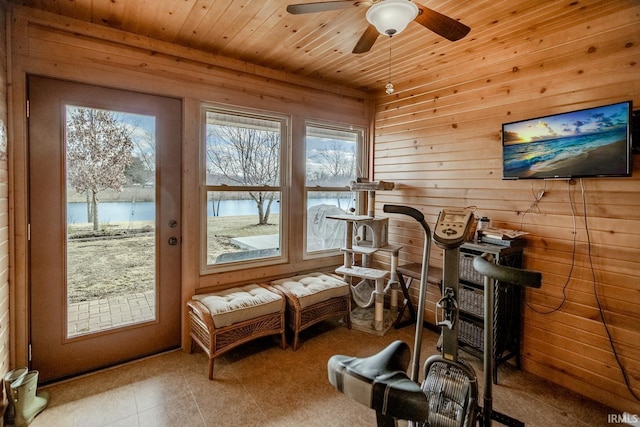 exercise area featuring ceiling fan, a water view, wooden ceiling, and wooden walls