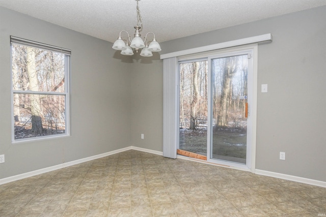 spare room featuring a healthy amount of sunlight, a textured ceiling, and a chandelier