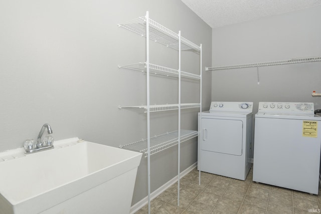 clothes washing area with sink, a textured ceiling, and washing machine and clothes dryer