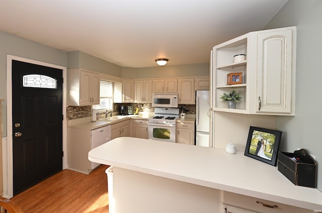 kitchen featuring sink, light wood-type flooring, kitchen peninsula, white appliances, and decorative backsplash