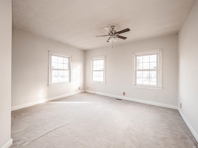 empty room with ceiling fan, light colored carpet, and a textured ceiling