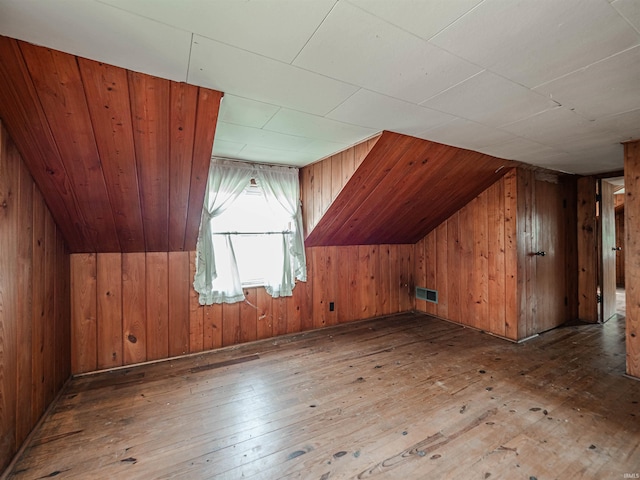 additional living space with wood-type flooring, vaulted ceiling, and wooden walls