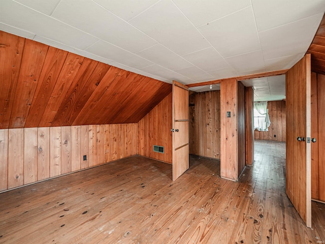 bonus room featuring lofted ceiling, hardwood / wood-style floors, and wooden walls