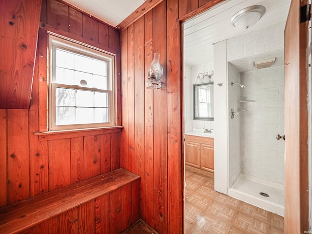 bathroom featuring parquet floors, vanity, wooden walls, and a tile shower