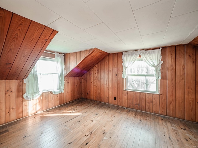 additional living space featuring lofted ceiling, a healthy amount of sunlight, hardwood / wood-style floors, and wood walls