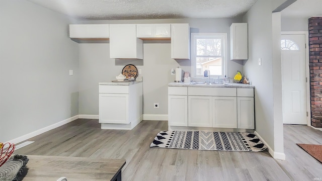 kitchen featuring white cabinetry, sink, light hardwood / wood-style floors, and a textured ceiling