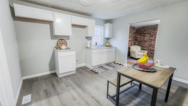 kitchen with sink, light hardwood / wood-style floors, a textured ceiling, and white cabinets