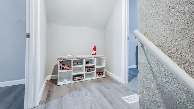 game room with vaulted ceiling, a textured ceiling, and light hardwood / wood-style floors