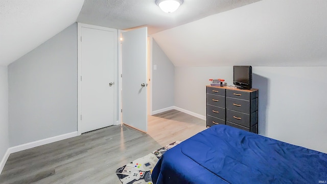 bedroom featuring lofted ceiling, hardwood / wood-style floors, and a textured ceiling