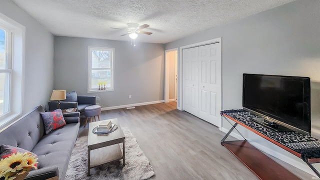 living room featuring ceiling fan, light hardwood / wood-style flooring, and a textured ceiling