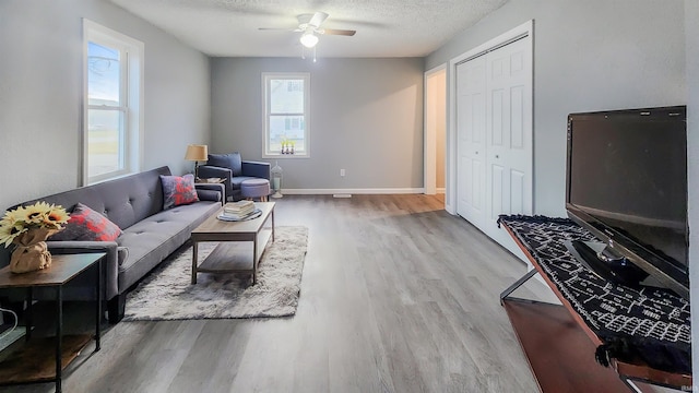 living room featuring ceiling fan, a textured ceiling, and light wood-type flooring