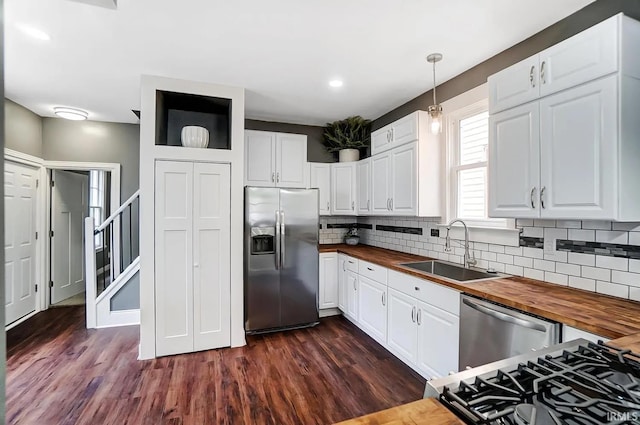 kitchen with decorative light fixtures, white cabinetry, butcher block counters, sink, and stainless steel appliances