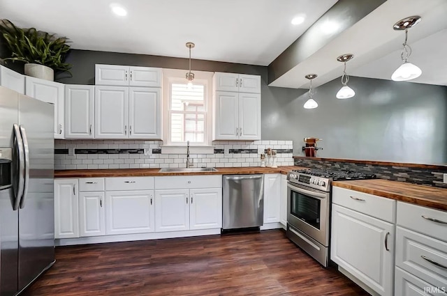 kitchen featuring appliances with stainless steel finishes, wood counters, sink, white cabinets, and hanging light fixtures