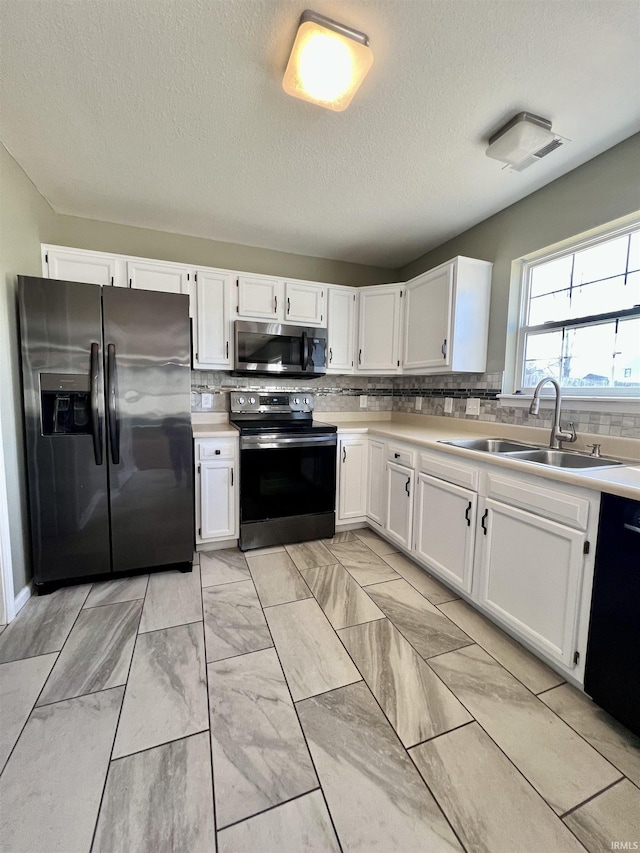 kitchen featuring appliances with stainless steel finishes, white cabinetry, sink, decorative backsplash, and a textured ceiling