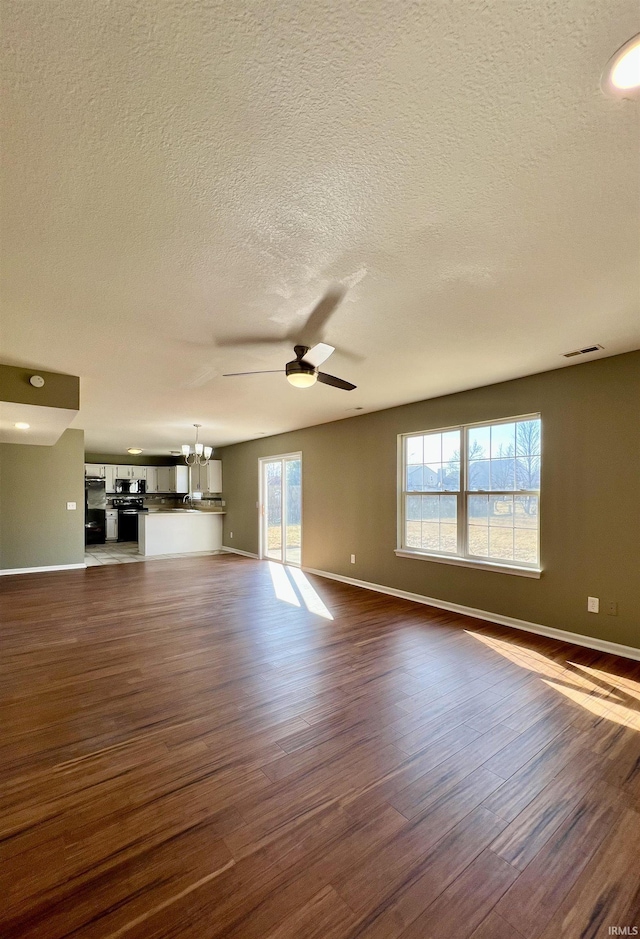 unfurnished living room featuring dark hardwood / wood-style flooring, ceiling fan with notable chandelier, and a textured ceiling