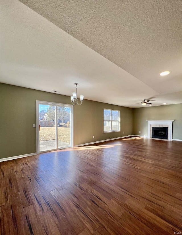 unfurnished living room featuring wood-type flooring, a tiled fireplace, ceiling fan with notable chandelier, and a textured ceiling