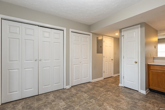 unfurnished bedroom featuring two closets, electric panel, and a textured ceiling