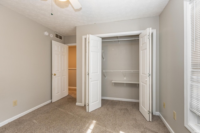 unfurnished bedroom featuring ceiling fan, light colored carpet, a closet, and a textured ceiling