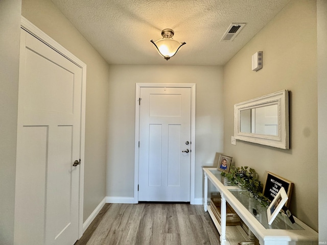 doorway with light hardwood / wood-style floors and a textured ceiling