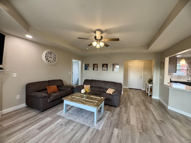 living room featuring light hardwood / wood-style floors, a raised ceiling, and ceiling fan