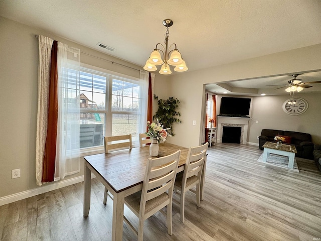 dining area with ceiling fan with notable chandelier, light hardwood / wood-style flooring, and a textured ceiling