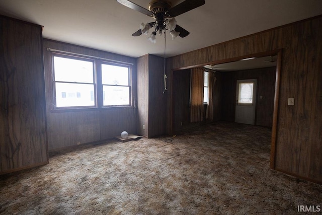 carpeted spare room with ceiling fan and wooden walls